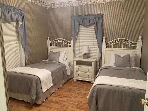 A bedroom with two beds, a nightstand with a lamp, and a window with curtains. - Beautiful lakefront home W/Breathtaking view (Claremont)