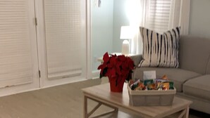 A living room with a wooden coffee table, a red potted plant, and a sofa with a zebra-patterned pillow.