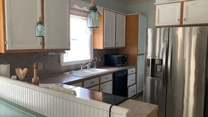 A kitchen with white cabinets, a stainless steel refrigerator, a microwave, and a sink.