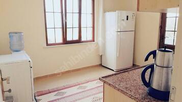 A kitchen with a refrigerator, a water dispenser, a kettle, and a window with curtains.