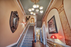 Eine prachtvolle Treppe mit einem Chandelier, einem hölzernen Kleiderständer und einem gerahmten Bild an der Wand.