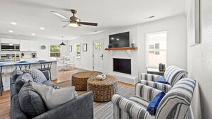A modern living room with a fireplace, striped sofas, and a dining area with a kitchen in the background. - 4 bedroom pool home 1 block from the Beach! (Myrtle Beach)