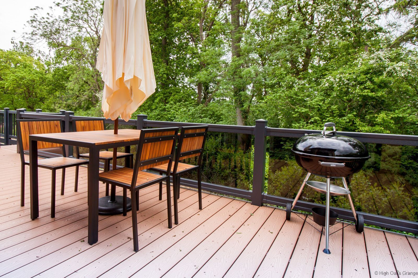 A wooden deck with a table and chairs, a grill, and an umbrella.