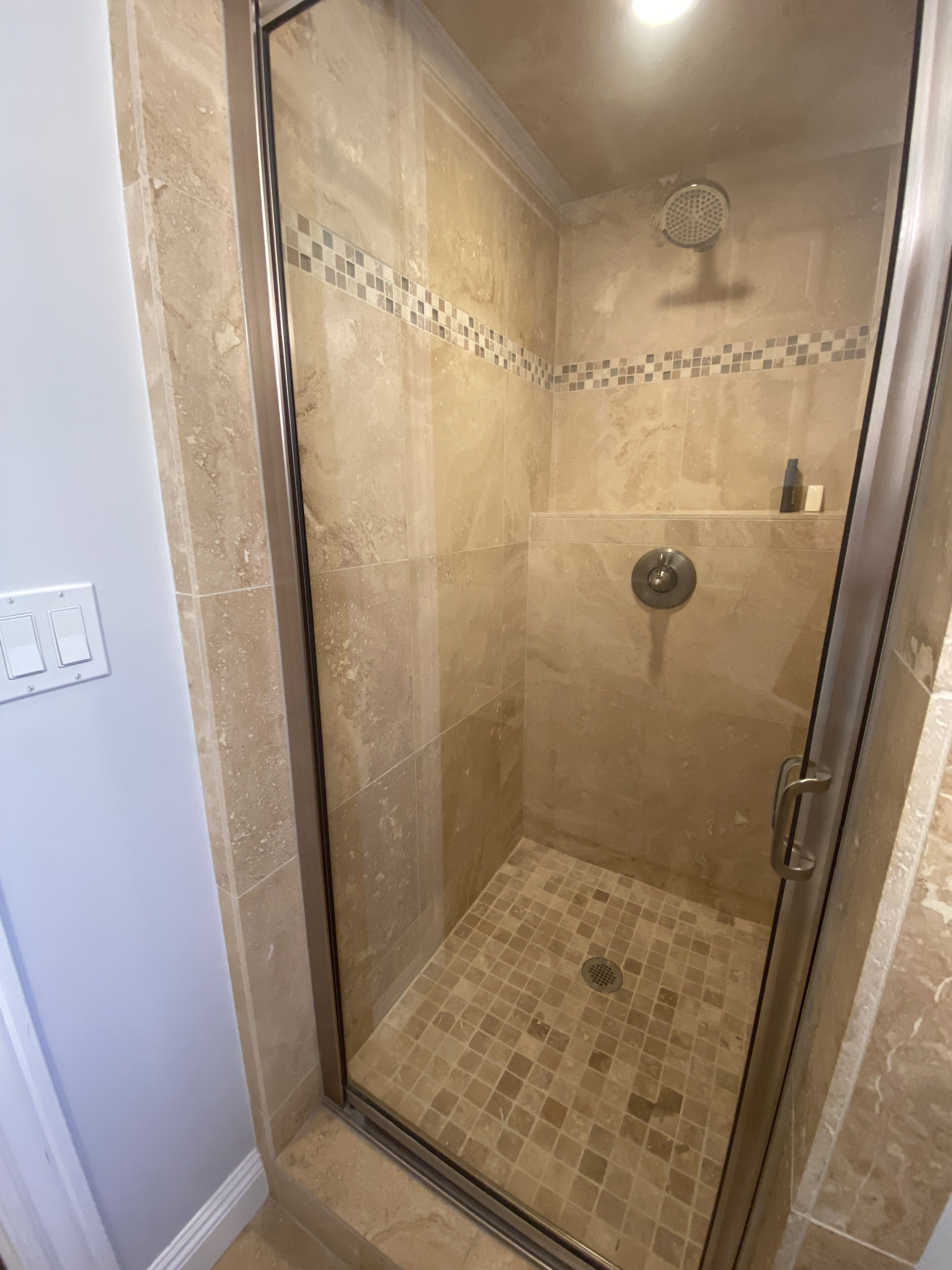 A glass-enclosed shower with a tiled floor and a showerhead.