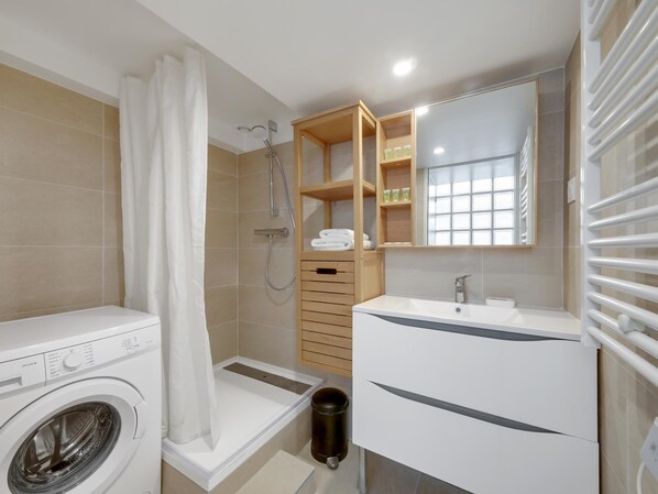 A modern bathroom with a washing machine, a shower, a sink with a mirror, and a wooden cabinet with toiletries. - Large luxury Loft for 6 people by Weekome (Paris)