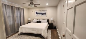 A neatly arranged bedroom with a bed, two bedside tables, a ceiling fan, and a framed artwork on the wall.