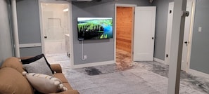 Un salon avec un téléviseur fixé au mur, un canapé avec des coussins et une porte en bois donnant sur une autre pièce.
