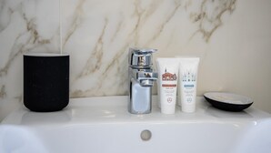 A bathroom sink with a marble backsplash, a black mug, a silver faucet, and two white tubes of body wash and shampoo.