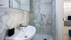 A modern bathroom with a marble shower enclosure, a white sink, and a black mug.