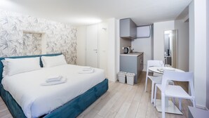 A modern hotel room with a bed, a small kitchenette, a dining area, and a bathroom.