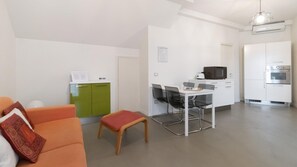 Ein kompakter Wohnbereich mit Küchenzeile, Essbereich und einer Sitzecke mit Sofa und kleinem Tisch.