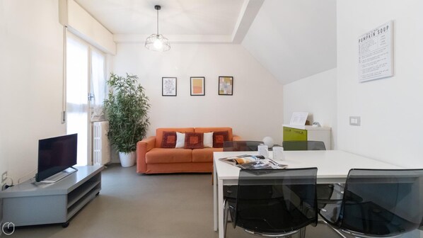 Ein modernes Wohnzimmer mit Fernseher, einem orangefarbenen Sofa, einem Esstisch und Stühlen.