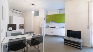 A modern kitchen with white and green cabinets, a dining area with a table and chairs, and a TV on a stand. - Italianway Easy - Plinio 64 (Milan)