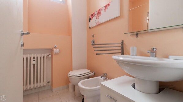 Et badeværelse med toilet, bidet, radiator og håndvask med spejl over.