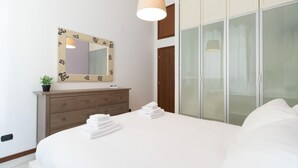 A hotel room with a large bed, a wooden dresser, a mirror with a floral frame, and a wardrobe with frosted glass doors. - Italianway Easy - Pisino 5 (Milan)