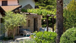 A stone building with a tiled roof, outdoor seating, and lush greenery. - Villa Charme 6 in Pollina (Pollina)