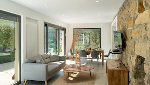 A modern living room with a sofa, coffee table, dining area, and stone wall. - Villa Charme 6 in Pollina (Pollina)