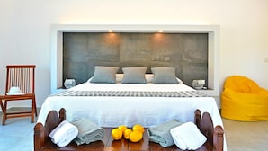 A modern bedroom with a large bed, a wooden chair, a yellow bean bag, and towels on a table. - Villa Charme 6 in Pollina (Pollina)