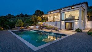 Uma casa moderna com dois andares, piscina, área de estar externa e um pátio bem iluminado.