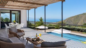 A modern outdoor terrace with wicker furniture, a pool, and a scenic ocean view.