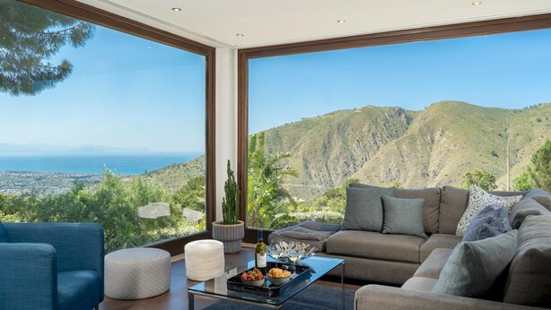Sala de estar moderna com uma grande janela com vista para uma paisagem montanhosa e o mar.