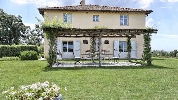 A two-story house with a covered patio, a garden, and a view of the sea.