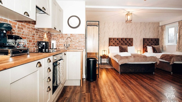 Una habitació d'hotel moderna amb sòl de fusta, un llit gran amb capçalera amb borrons, una tauleta de nit amb una làmpada i vistes a l'exterior per una finestra.