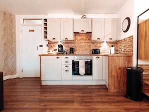 A compact kitchen with white cabinets, a brick backsplash, and a wooden countertop.