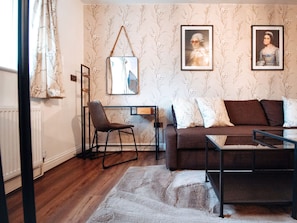A modern living room with a brown sofa, a glass coffee table, a small desk with a chair, and two framed pictures on the wall.