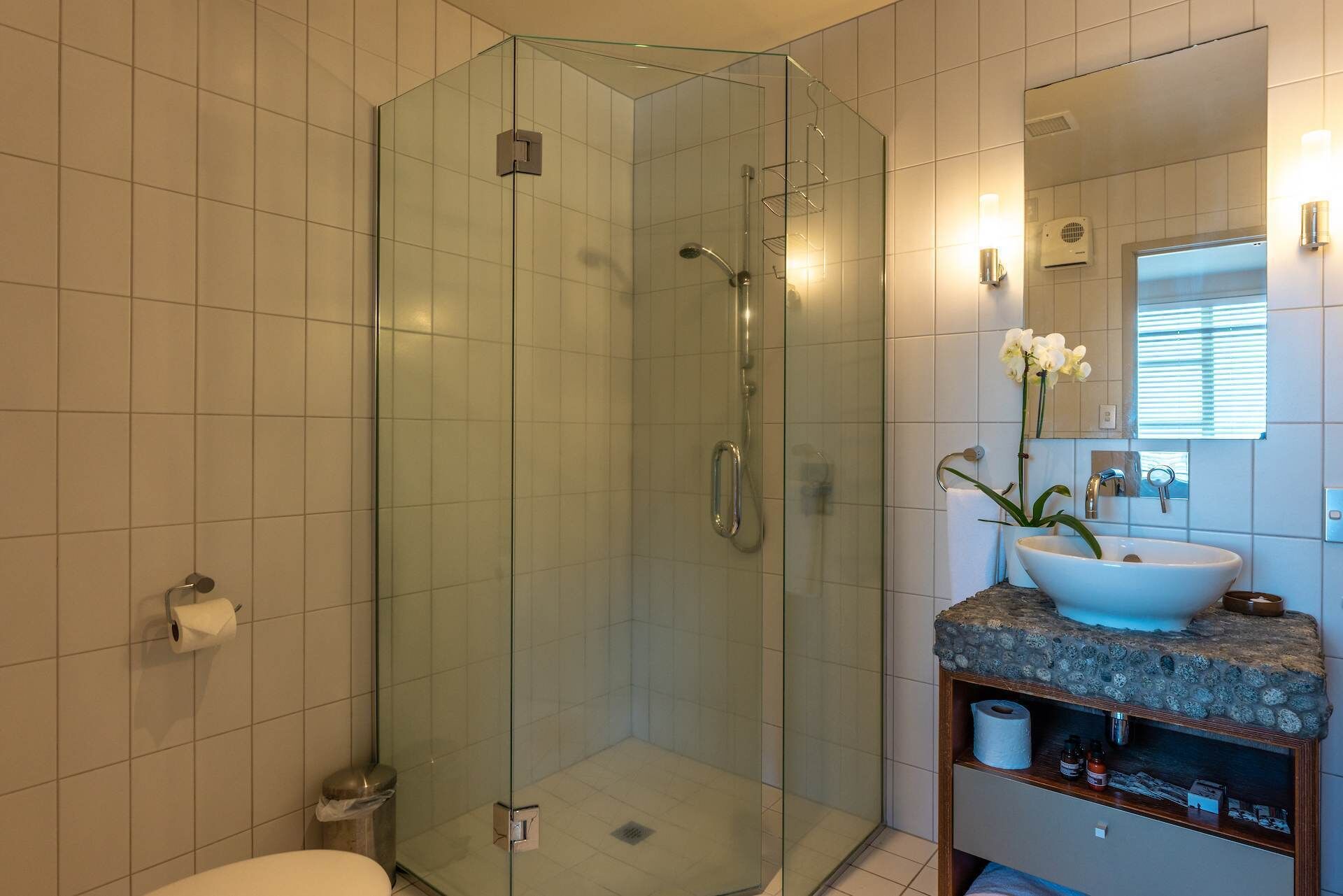 A modern bathroom with a glass-enclosed shower, a white sink with a stone countertop, and a mirror with a window above it.