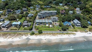 An aerial view of a coastal residential area with houses, a beach, and a large building complex. - The Sands - Apartment 12 Onetangi Beach (Waiheke Island)