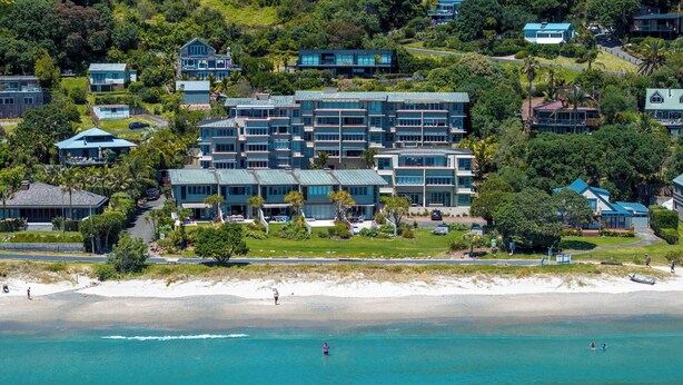 A coastal hotel with multiple buildings, a beach, and clear blue waters. - The Sands - Apartment 12 Onetangi Beach (Waiheke Island)