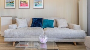 Un salón con un sofá gris, dos cojines y una mesa de centro de cristal con una esfera decorativa. Tres cuadros enmarcados cuelgan de la pared.
