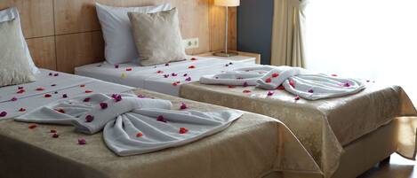 Two twin beds with beige linens, a wooden headboard, a bedside lamp, and a window with curtains.