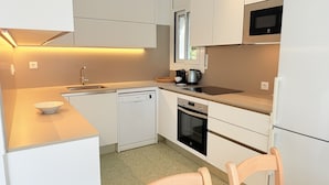 A compact kitchen with a dishwasher, oven, microwave, and a small dining area with a chair. - Ore05 (Rosas / Roses)