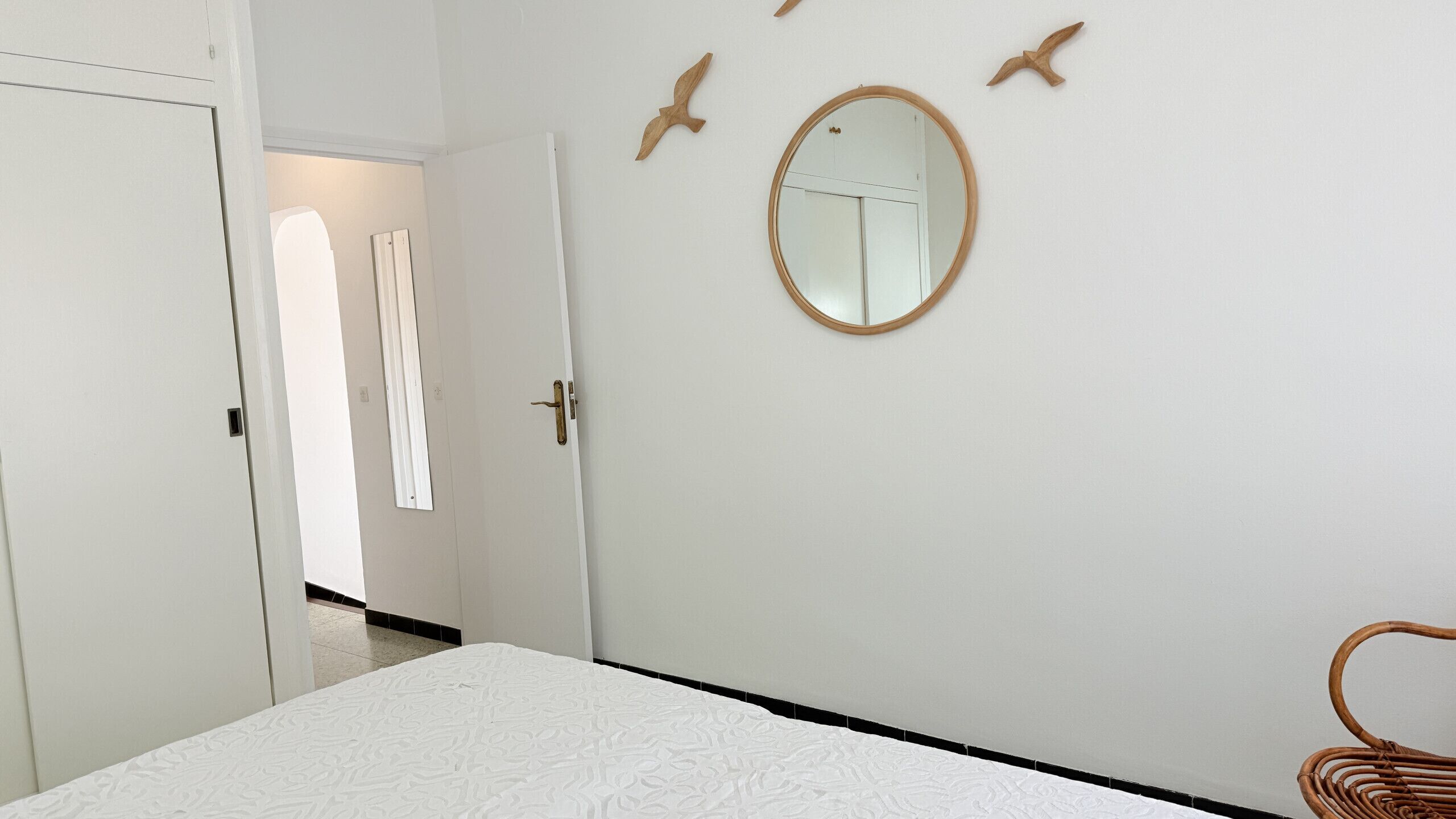 Une chambre à coucher comprenant un lit, une porte, un miroir et une décoration murale représentant un oiseau.