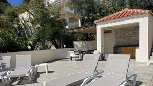 A rooftop terrace with lounge chairs, a dining area, and a stone wall. - Ore05 (Rosas / Roses)