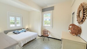 A bedroom with a bed, two windows, a chair, and a decorative wall piece. - Ore05 (Rosas / Roses)