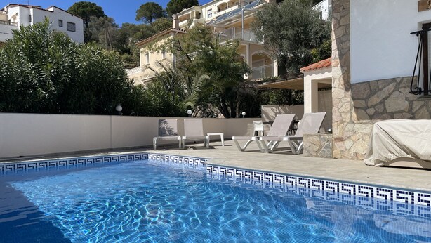 A swimming pool with clear blue water, surrounded by lounge chairs and a stone wall. - Ore05 (Rosas / Roses)