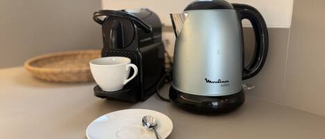 A coffee maker, a cup, and a plate with a spoon on a kitchen counter.