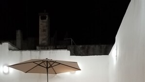 Un patio al aire libre con una mesa y sillas blancas, una sombrilla y un suelo de baldosas.
