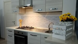 Una cocina moderna con estufa a gas, horno, pileta y armarios blancos. Hay un salpicadero de ladrillo y un florero con flores amarillas en la encimera.