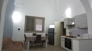 Una cocina compacta con armarios blancos, una zona de comedor con mantel estampado y un sofá con funda de estampado de leopardo.