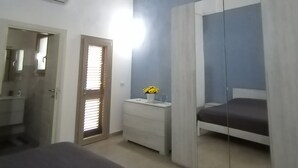 Un dormitorio con cama, mesita de noche con lámpara, armario y aire acondicionado en la pared.