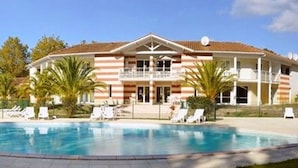 A two-story building with a swimming pool, balconies, and palm trees. - Vacation home in Soulac near the ocean (Soulac-sur-Mer)