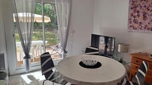 A dining area with a round table, chairs, a TV, and a lamp. - Vacation home in Soulac near the ocean (Soulac-sur-Mer)