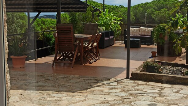 A covered patio area with stone flooring, outdoor furniture, and potted plants. - Casa de invitados adaptada. (Santa cristina d'Aro)