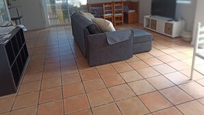 A living room with a sofa, ottoman, and a TV. There is a dining table and chairs in the background. - Casa de invitados adaptada. (Santa cristina d'Aro)