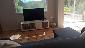 A living room with a TV on a white cabinet, a couch, and a sliding glass door leading to an outdoor area. - Casa de invitados adaptada. (Santa cristina d'Aro)