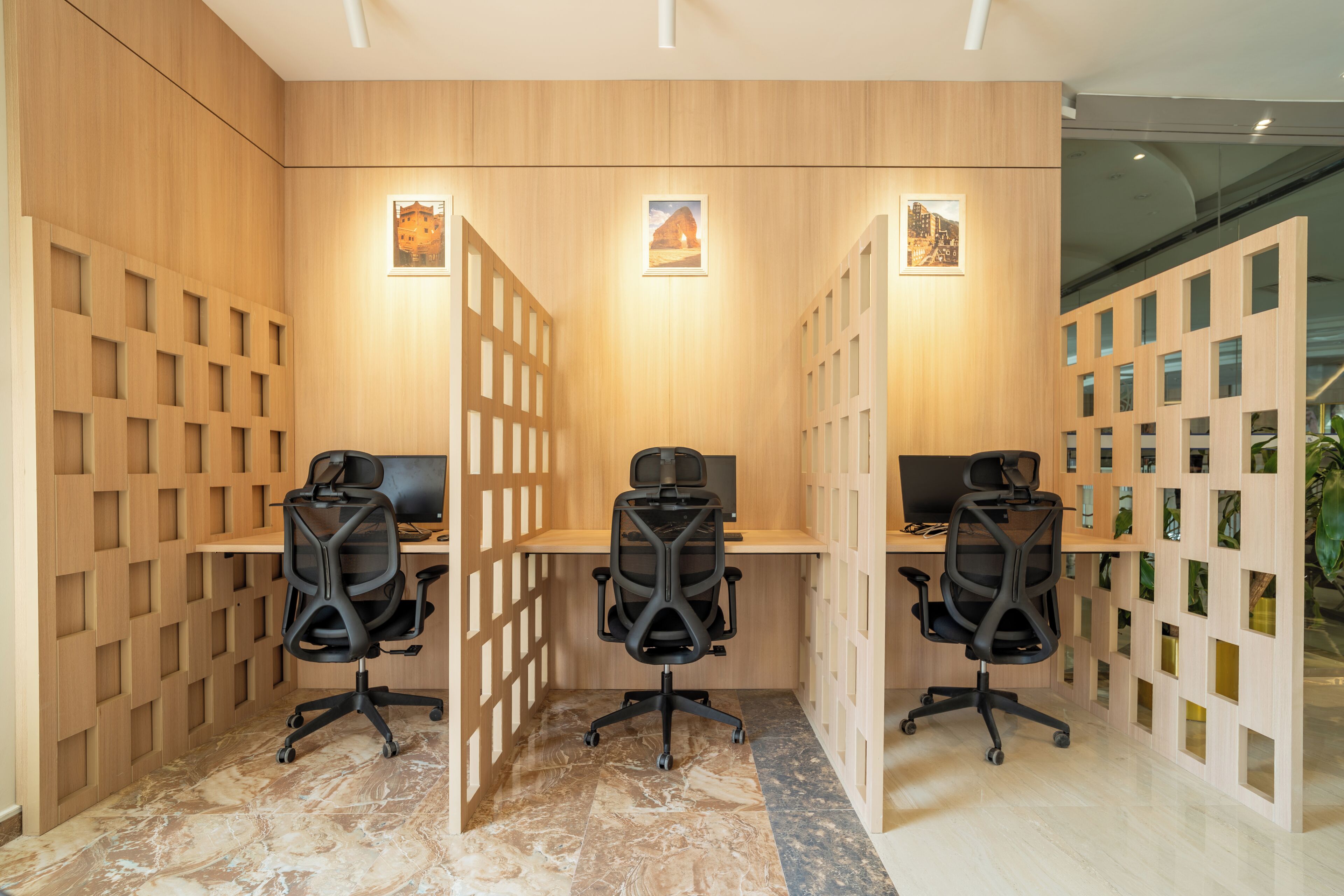 Un espace de bureau moderne comprenant trois bureaux, chacun équipé d’un fauteuil de bureau noir, et une cloison en bois avec des panneaux ajourés.